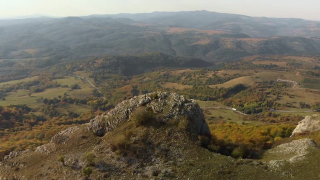 Tracking aerial shot over rocky hill, valley and forest as background