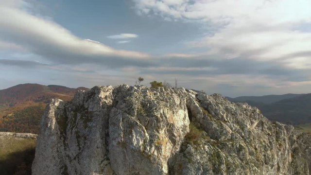 Tracking aerial shot over rocky hill, mountain and forest as background