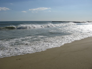 Playa de Barcelona, arena gris y olas bajo del cielo azul y nubes blancos