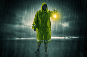 Raincoated man walking in storm with glowing lantern in his hand
