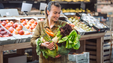 Woman in the supermarket. Beautiful young woman shopping in a supermarket and buying fresh organic vegetables