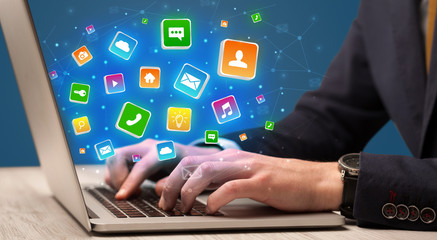 Businessman hand typing on laptop with flying application icons around
