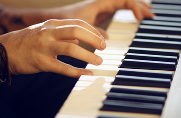 Fototapeta premium On a musical keyboard instrument, which is illuminated by the sun, a man plays a melody with his hands. On hand to wear the bracelet.