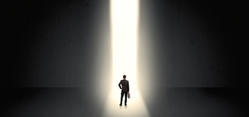 Businessman standing and seeing the light at the end of a big wall
