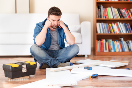 Sad Young Man Reading The Instructions To Assemble Furniture