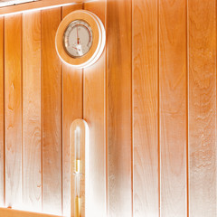 Round thermometer and hourglass on the wall of traditional sauna