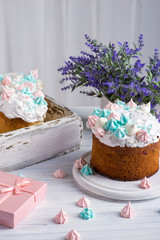 Tree tasty decorate Easter cakes lie on a round white wooden plate on a   white wooden table.  A tray with cakes and flowers  stand on the table.