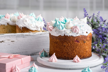 Tree tasty decorate Easter cakes lie on a round white wooden plate on a   white wooden table.  A tray with cakes and flowers  stand on the table.