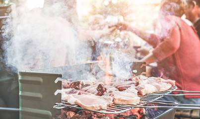 Family grilling meat for friends at bbq meal outdoor - Different age of people having fun at barbecue dinner - Summer lifestyle, friendship and fun concept - Focus on left steak - obrazy, fototapety, plakaty