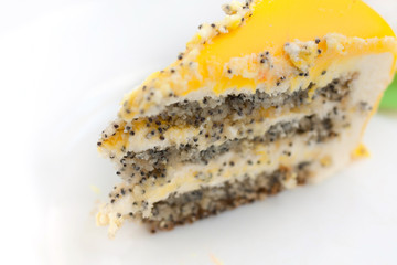 The slice of yellow poppy topping cake  on white plate with decor