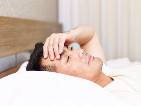 Asian Man Lying On Bed Hand On Forehead