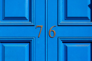 House number 76, with the seventy-six in bronze numerals on a blue painted wooden door