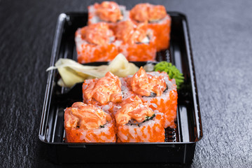 Spicy salmon makizushi roll with salmon in take-away container over slate plate background