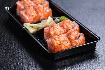 Spicy salmon makizushi roll in take-outcontainer over slate plate background