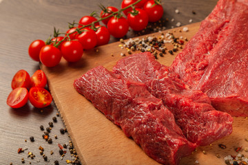 Raw beef on a wooden background with spices and vegetables.