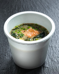 Miso salmon soup over slate plate background in take-out container