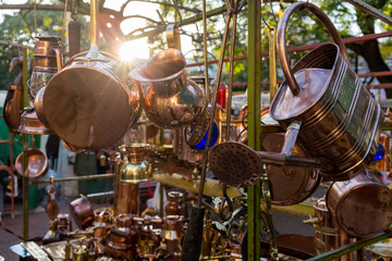 Vintage brass saucepans, jugs and watering can on a market stall at flea market in San Telmo,...