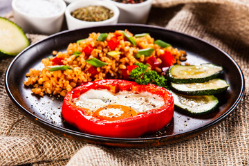 Fried egg, groats and vegetables on wooden table