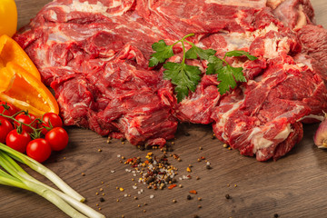 Raw beef on a wooden background with spices and vegetables.