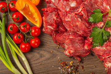 Raw beef on a wooden background with spices and vegetables.