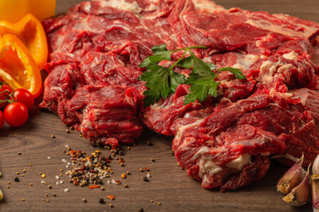 Raw beef on a wooden background with spices and vegetables.