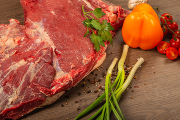 Raw beef on a wooden background with spices and vegetables.