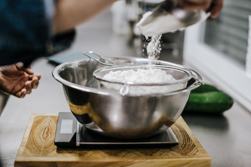 Bakery concept. Working woman weighing and sifting the ingredients of her sponge cake. Lifestyle.