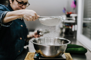Bakery concept. Working woman weighing and sifting the ingredients of her sponge cake. Lifestyle.