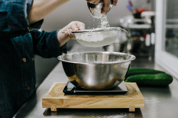 Bakery concept. Working woman weighing and sifting the ingredients of her sponge cake. Lifestyle.