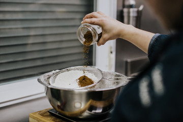 Bakery concept. Working woman weighing and sifting the ingredients of her sponge cake. Lifestyle.