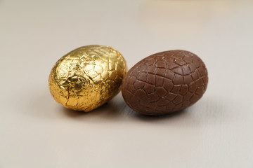Two chocolate eggs with and without golden paper for Easter