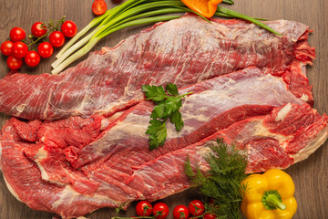 Raw beef on a wooden background with spices and vegetables.