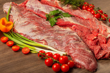Raw beef on a wooden background with spices and vegetables.