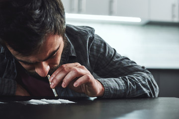 Drug addiction is a self-punishing disease that ruins mental, psychological and physical health. Man snorts a line of cocaine with a rolled up bank note. Close up