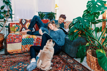 young happy couple with pet at home reading books - lifestyle, leisure, life together concept