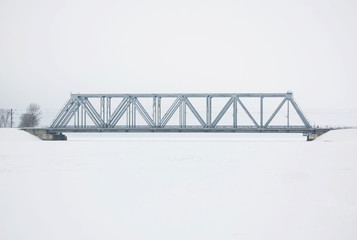 Railway bridge over the river in winter against the background of the cloudy sky