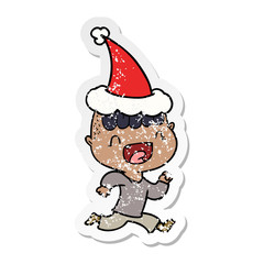 distressed sticker cartoon of a happy boy laughing and running away wearing santa hat