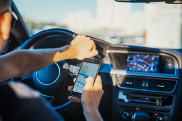 Close up of young man looking at GPS navigator behind the wheel in car.