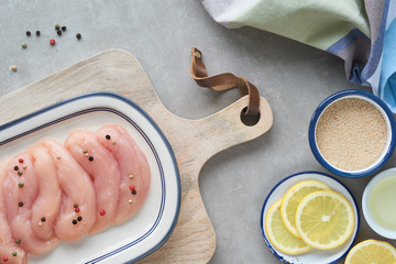 Raw chicken fillet. Meat with breadcrumbs, herbs , lemon and cooking oil. Top view on light stone