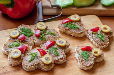heart shaped canape with liver pate, decorated with olives, sweet peppers and dill, cooking at home, close up