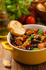 Traditional Italian caponata, served with croutons in a yellow, sunny pot. Decorated with basil and pine nuts.