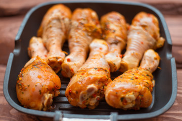 Raw chicken drumsticks in sauce and spices in a pan not a wooden background.