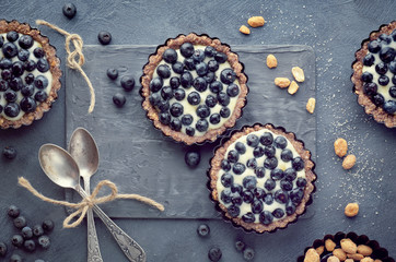 Top view on wholegrain blueberry tarts with vanilla cream on dark