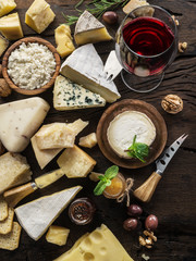 Cheese platter with organic cheeses, fruits, nuts and wine on wooden background. Top view. Tasty cheese starter.