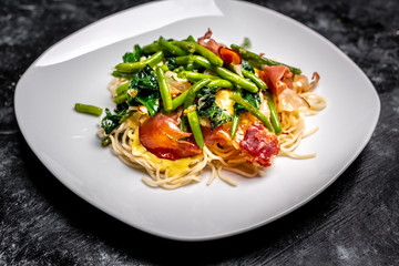 Spaghetti carbonara with pieces of crispy bacon, garlic, fresh spinach leaves and sprouts of green, young peas