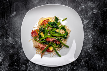 Spaghetti carbonara with pieces of crispy bacon, garlic, fresh spinach leaves and sprouts of green, young peas