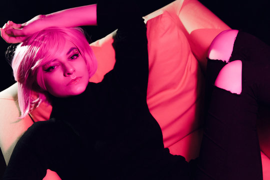 Fashion sexy woman pink hair on the armchair . Pink light. Life style. Retro wave neon noir lights color toningt