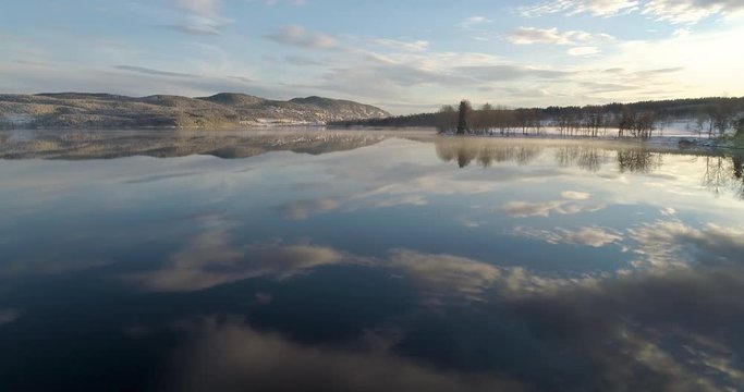 4K video with slide and tilt motion of lake with mist and reflections of cloudy sky in beautiful and vibrant sunset in Norway.