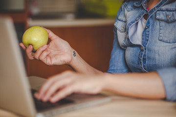 Woman having healthy snack while using laptop in kitchen. Close up
