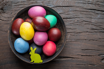 Colorful Easter eggs in bowl on wooden table. Attribute of Easter celebration.